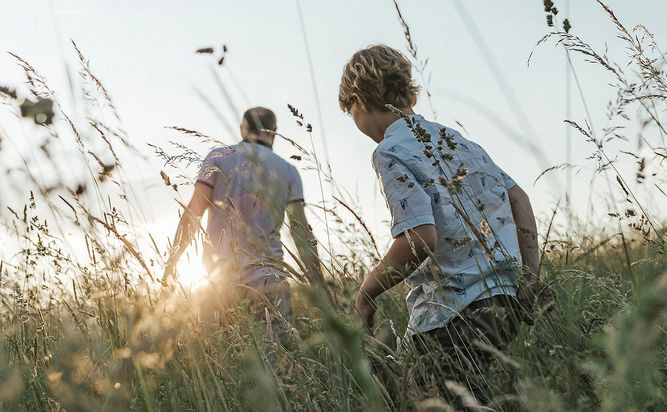 Two people walking through a grassy field with the sun setting in the background.