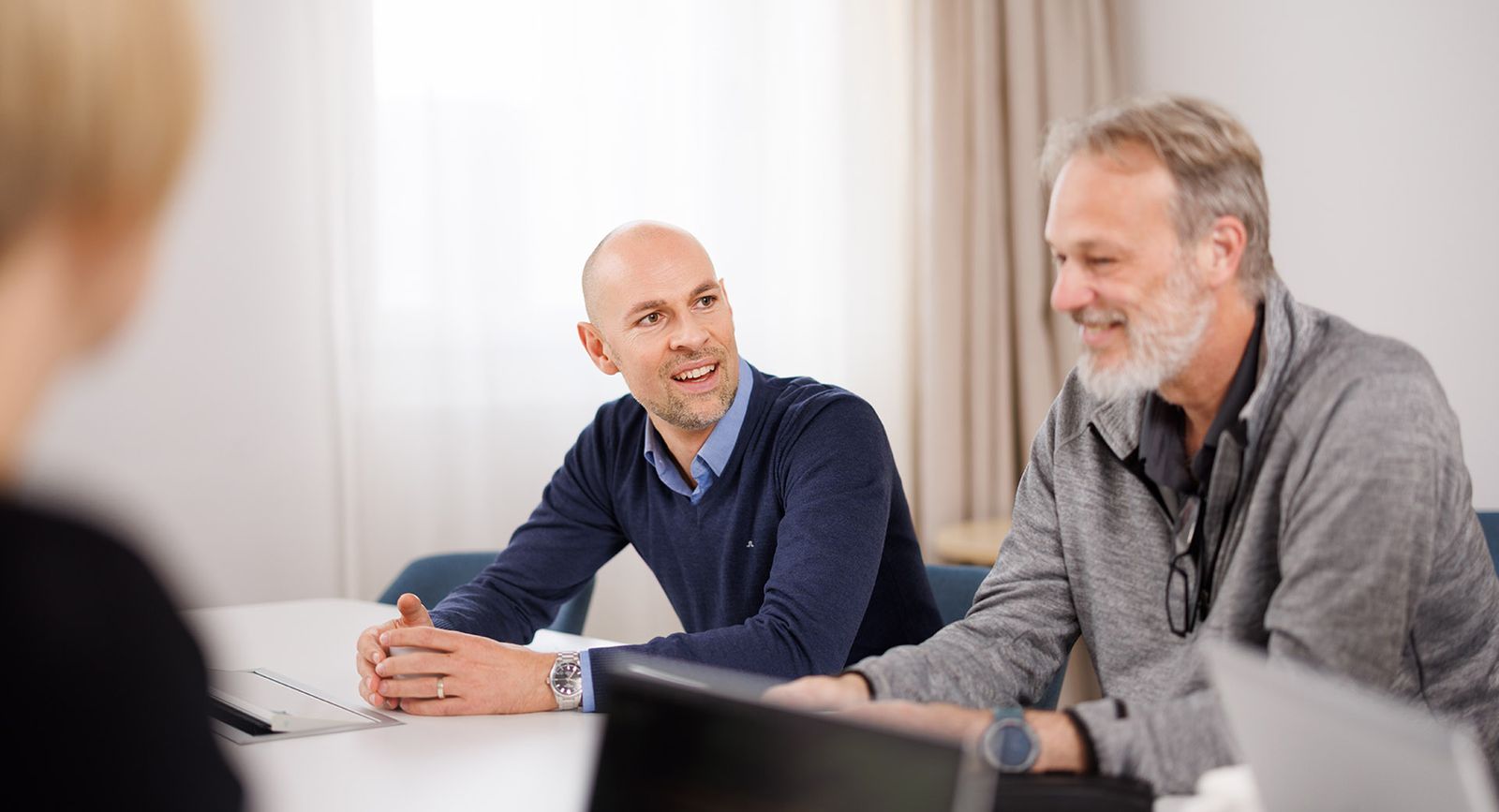 Three Camurus employees sit around a table in a bright room, engaged in a discussion. 